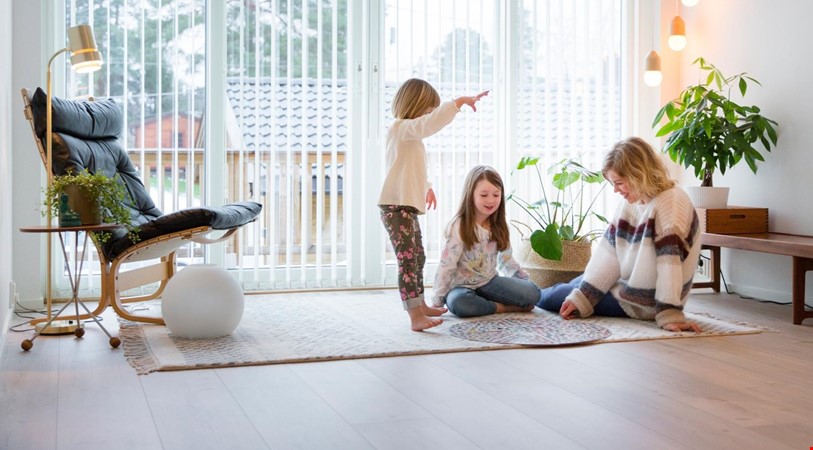 En kvinne og 2 barn som spiller brettspill på stuegulvet