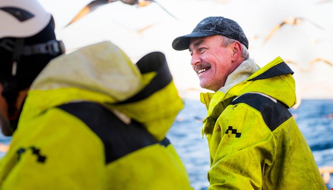 En smilende Jan Helge Iversen, fisker på MS Sundsbøen, ute på sjøen med måker flyvende i bakgrunnen.