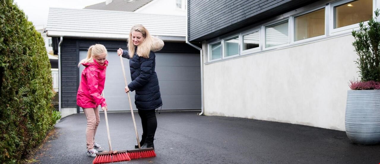Jente og en dame som koster asfalt utenfor en garasje