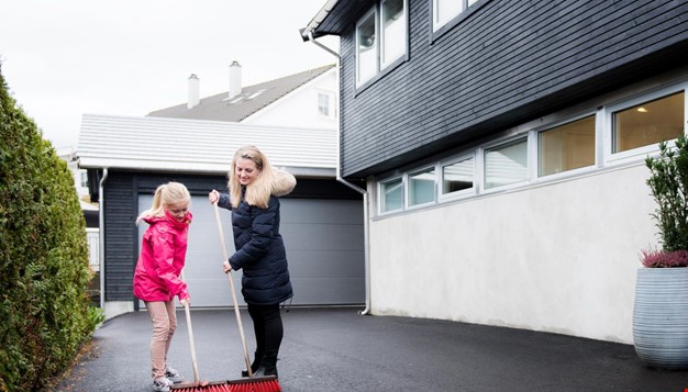 Jente og en dame som koster asfalt utenfor en garasje
