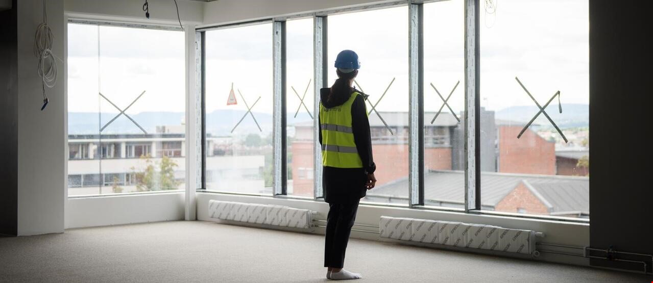 Person med refleksvest og hjelm som står i uferdig rom