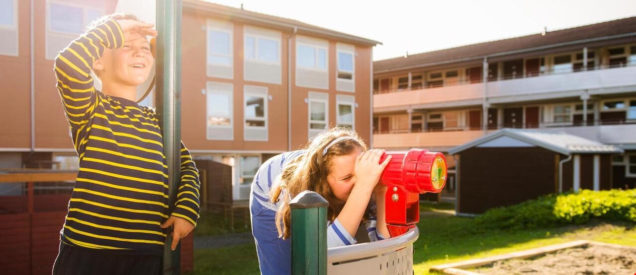2 barn som leker på lekeplass utenfor leiligheter