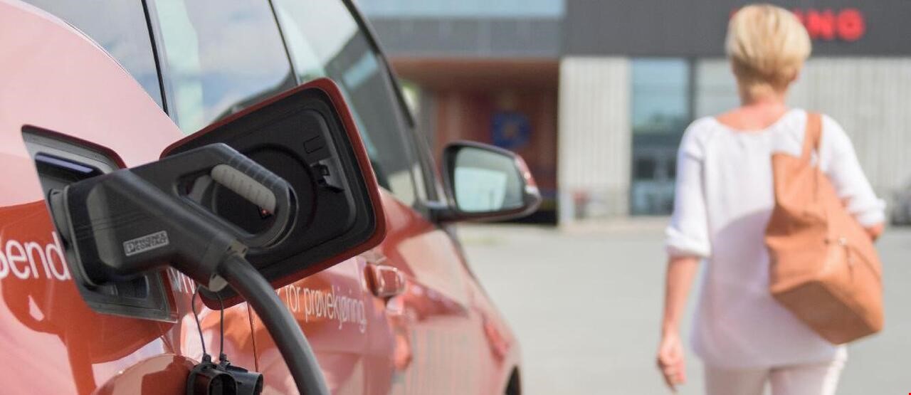 Person som går bort fra oransj bil som lader