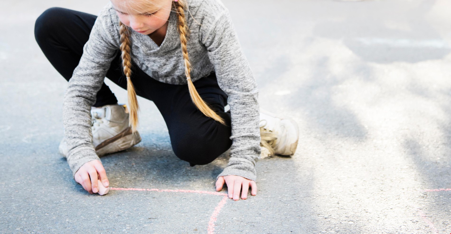 Jente som tegner med kritt på asfalt