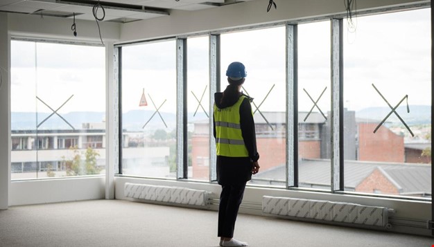 Person med refleksvest og hjelm som står i uferdig rom