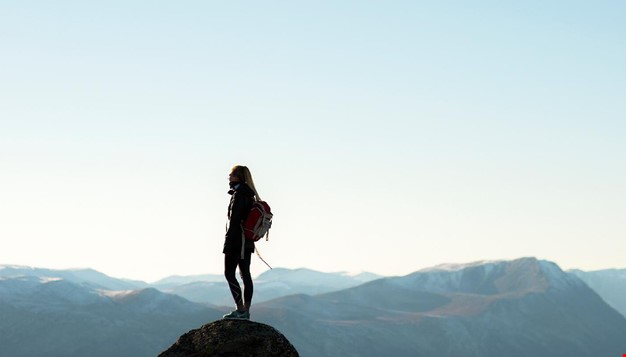 Person i siluett mot blå himmel, stående på en fjelltopp