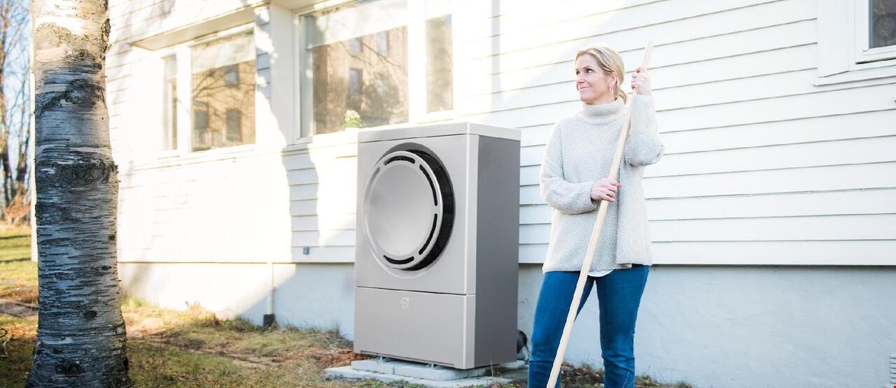 En kvinne som raker plenen ved huset sitt hvor det er installert en varmepumpe på utsiden