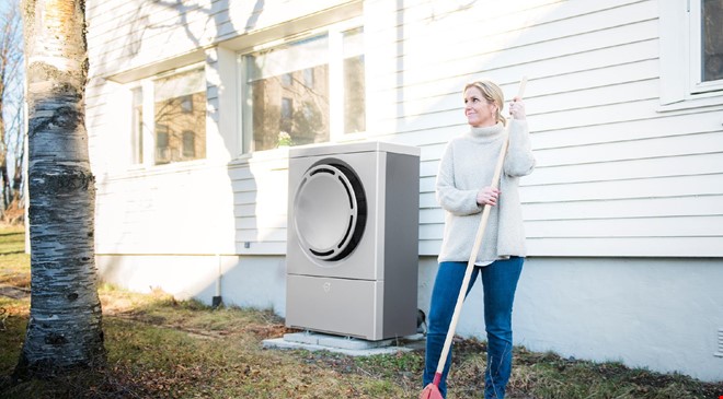 En kvinne som raker plenen ved huset sitt hvor det er installert en varmepumpe på utsiden