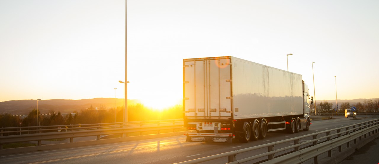 Hvit lastebil i trafikk under solnedgang
