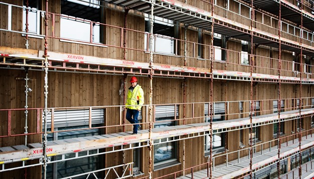 Person med refleksvest og hjelm i stilas utenfor et brukt bygg