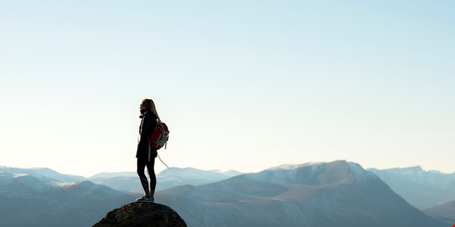 Person som står på toppan av et fjell med flere fjell i bakgrunnen
