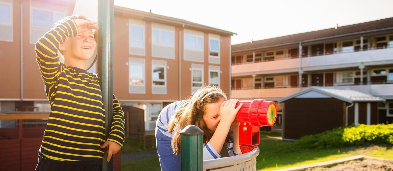 2 barn som leker på lekeplass utenfor leiligheter