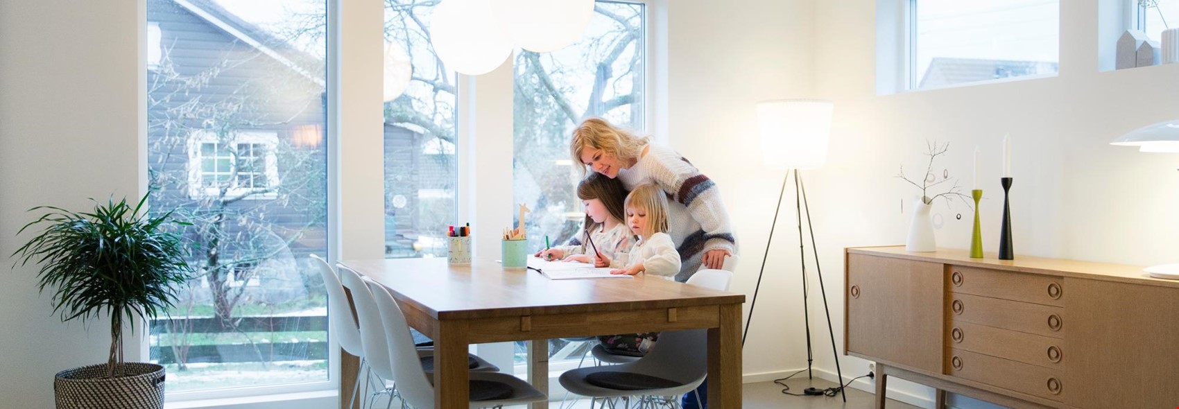 Kvinne som hjelper 2 barn med lekser på kjøkkenbordet