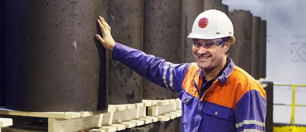 Person i arbeidsklær og hjelm som smiler og holder på et stort betongrør