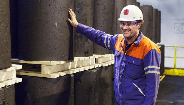 Person i arbeidsklær og hjelm som smiler og holder på et stort betongrør