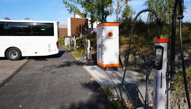 Baksiden av en hvit buss og ladestasjoner