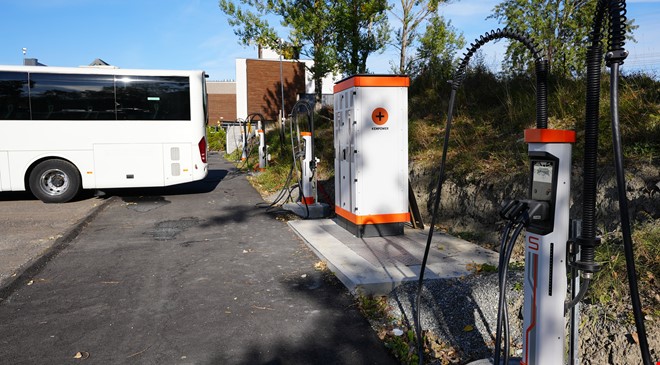 Baksiden av en hvit buss og ladestasjoner