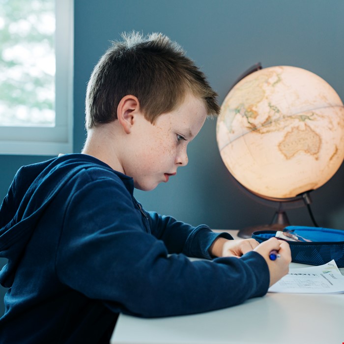 Marius som gjør lekser ved et skrivebord omgitt av nymalte grå-blå vegger.