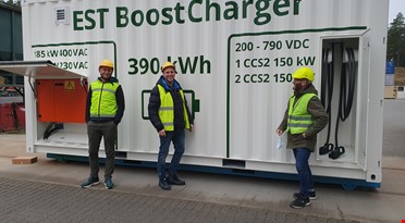 En gruppe menn  som står foran en hvit beholder med grønn tekst som ser ut til å være et batteri